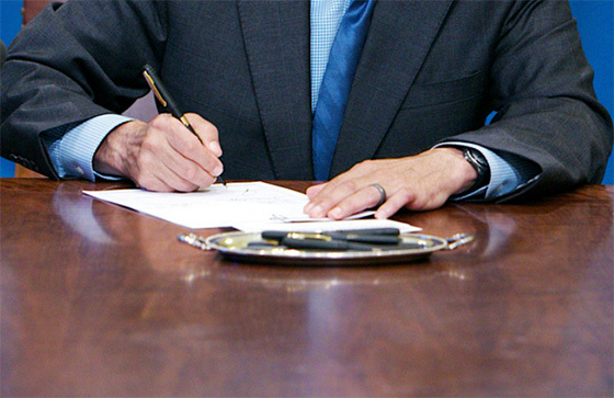 Hand placing bill documents in to a wooden box labeled 'hopper'