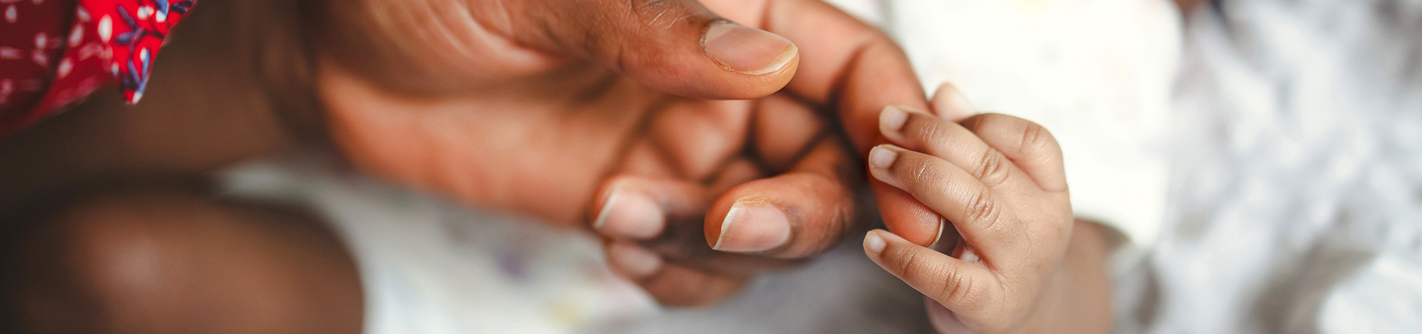 A baby's hand holds onto the finger of a parent's hand.